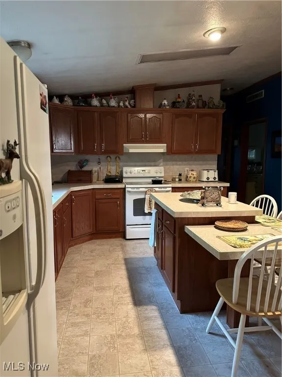 Kitchen with white electric range oven, fridge, exhaust hood, light countertops, and a kitchen bar