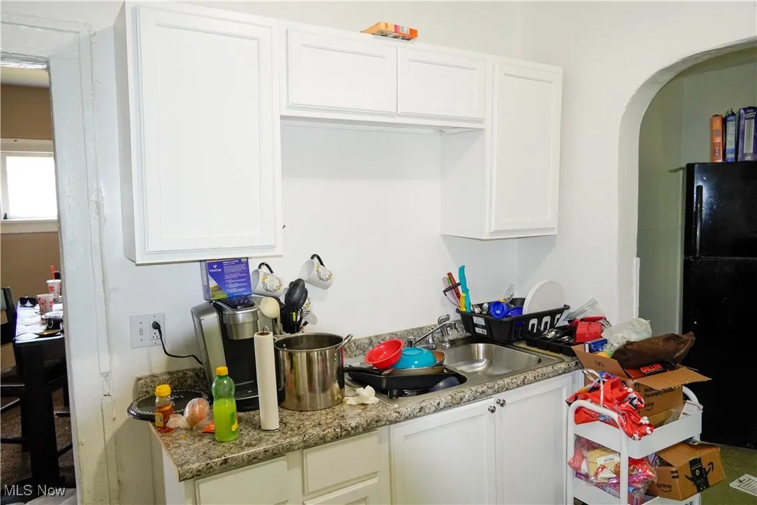 Kitchen featuring freestanding refrigerator, white cabinets, a sink, and arched walkways