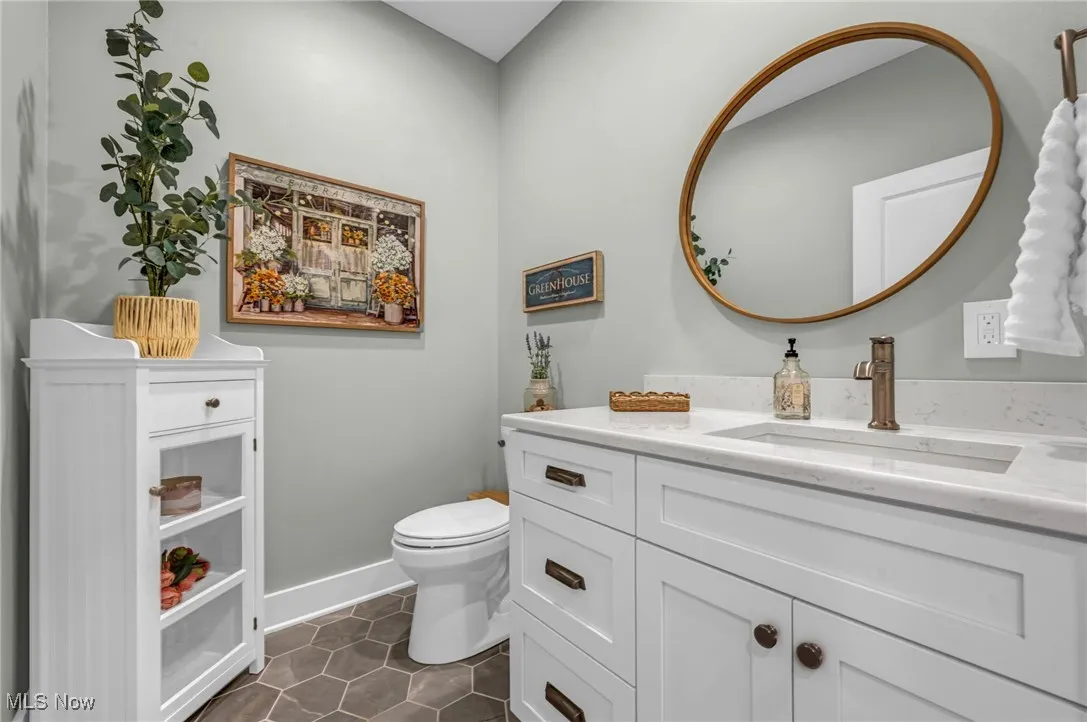 Half bathroom with toilet, vanity, tile patterned flooring, and baseboards