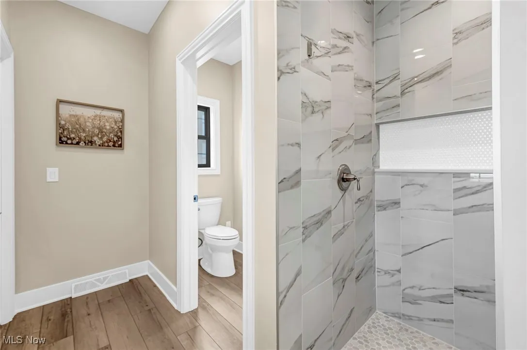 Full bath with tiled shower, wood finished floors, toilet, and baseboards