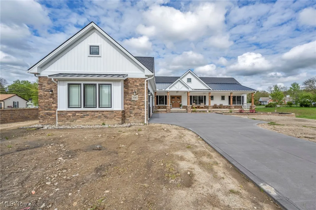 Modern inspired farmhouse with a standing seam roof, a porch, stone siding, metal roof, and board and batten siding