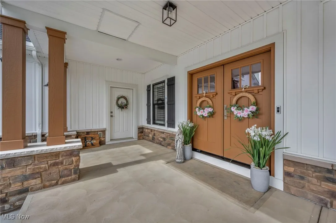 View of exterior entry featuring covered porch, board and batten siding, and stone siding