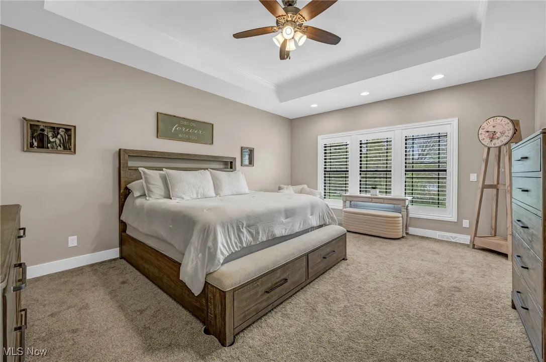 Carpeted bedroom with a tray ceiling, recessed lighting, baseboards, crown molding, and a ceiling fan