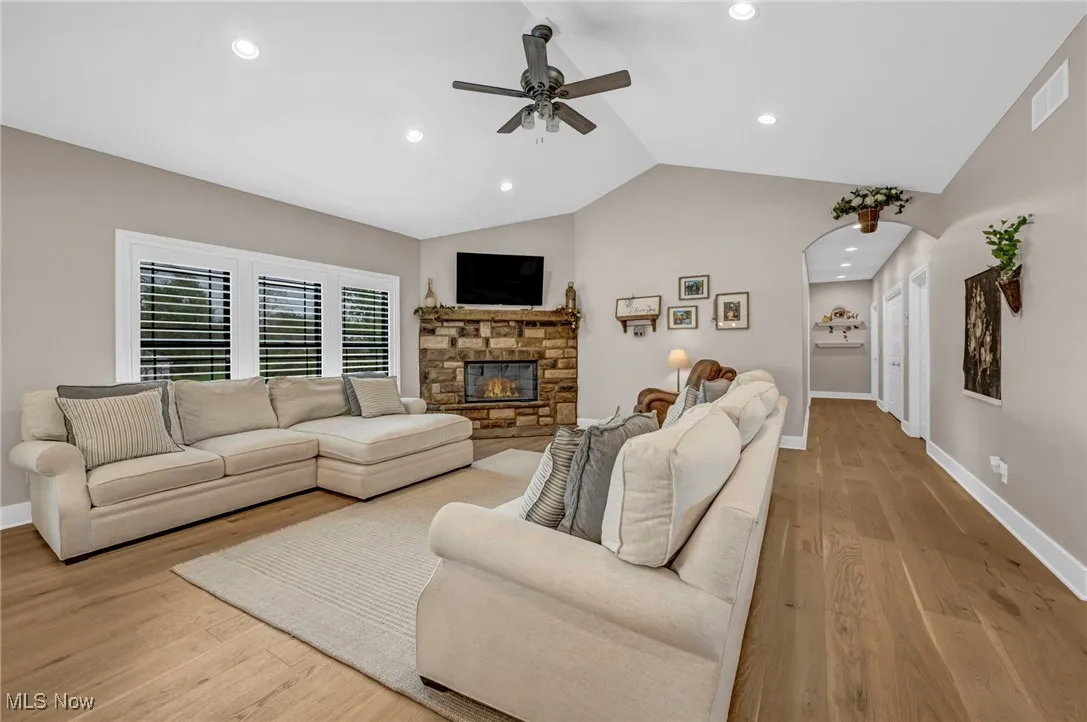 Living area with ceiling fan, lofted ceiling, baseboards, arched walkways, and wood finished floors