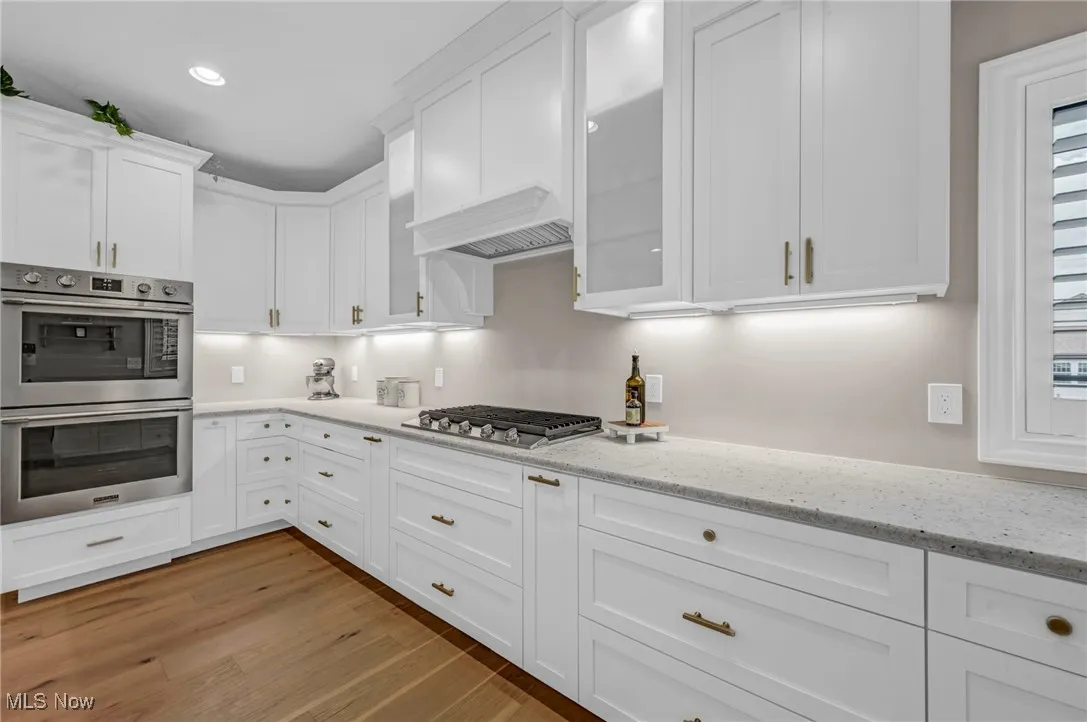 Kitchen featuring stainless steel appliances, white cabinets, light wood-type flooring, light stone counters, and recessed lighting