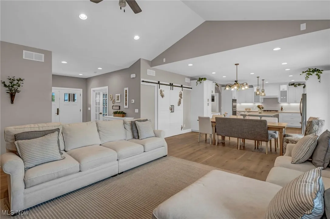 Living room featuring a barn door, ceiling fan, light wood-style flooring, vaulted ceiling, and recessed lighting