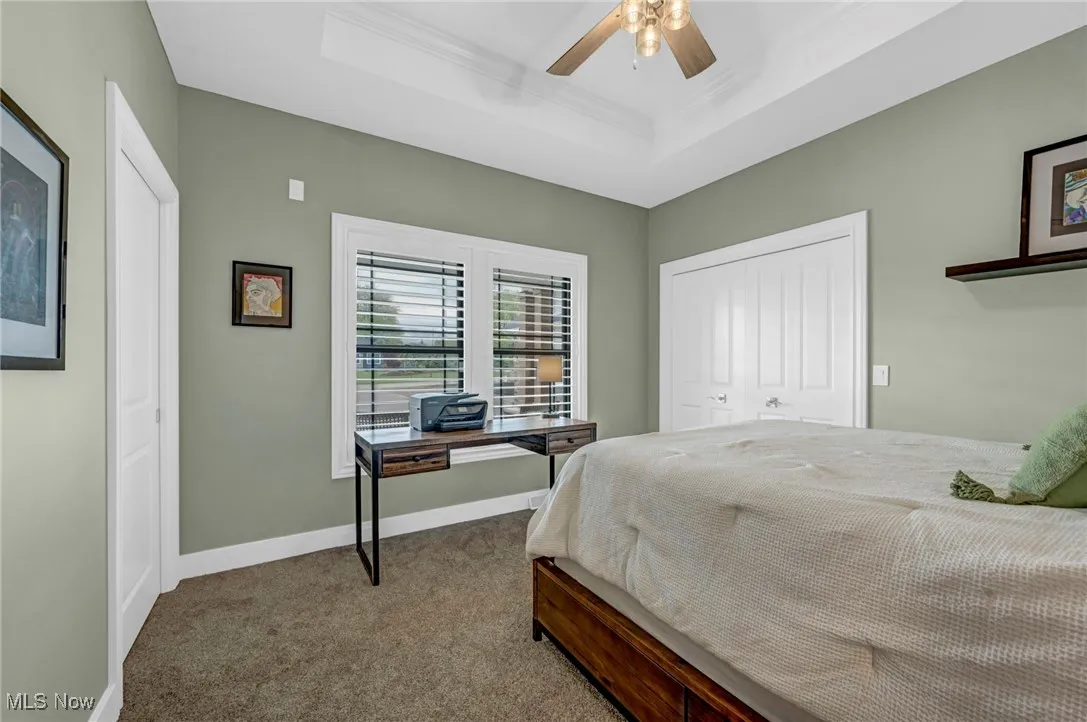 Bedroom with carpet floors, a tray ceiling, ornamental molding, baseboards, and a ceiling fan