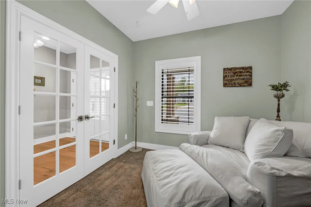 Living area with french doors, dark colored carpet, ceiling fan, and baseboards