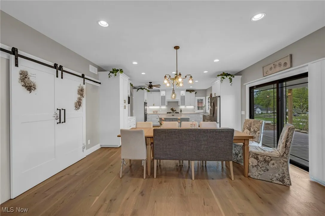 Dining room with a barn door, light wood-style flooring, a chandelier, recessed lighting, and baseboards