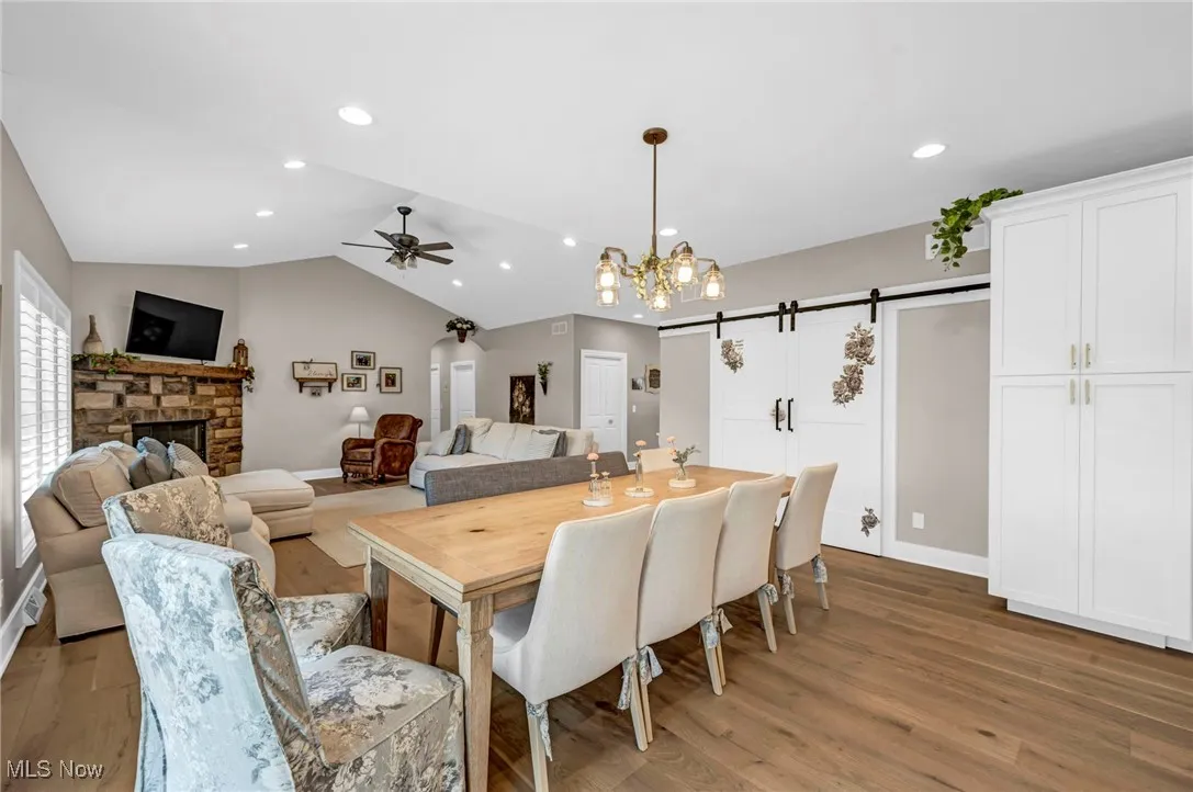 Dining room with light wood-style floors, a ceiling fan, a stone fireplace, a chandelier, and lofted ceiling
