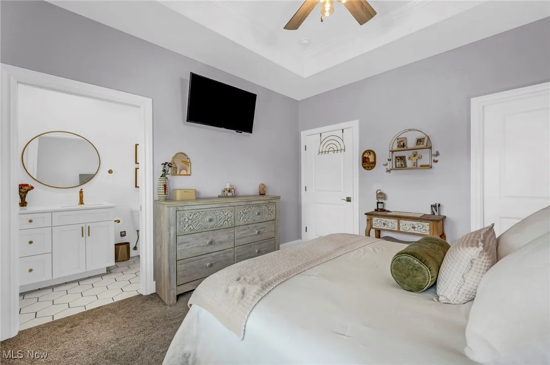 Bedroom with light carpet, a sink, crown molding, ensuite bath, and ceiling fan