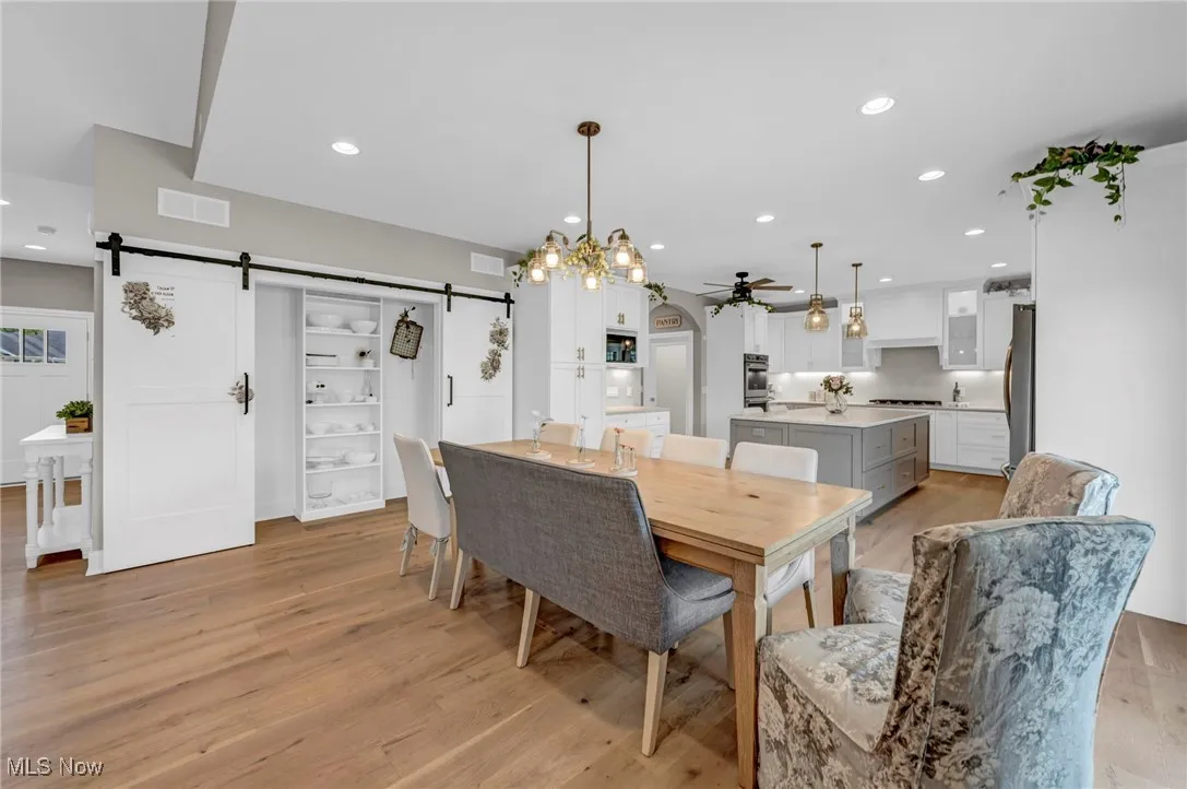 Dining room featuring a barn door, a ceiling fan, light wood finished floors, and recessed lighting