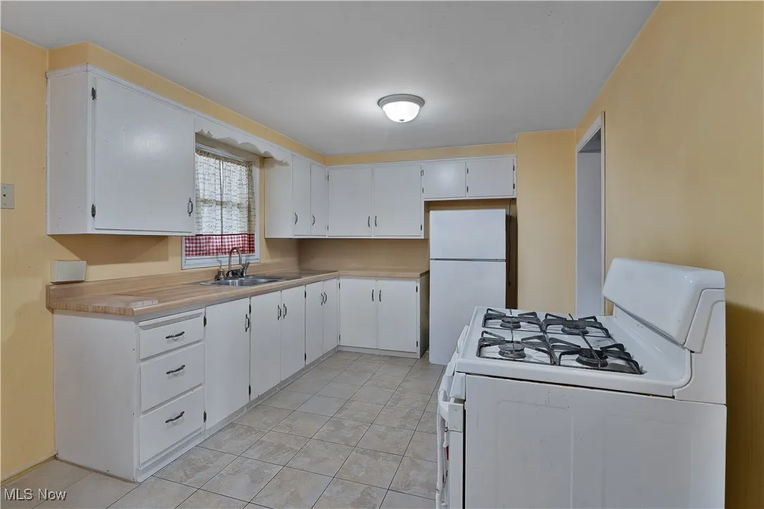 Kitchen featuring white appliances, a sink, light tile patterned floors, and white cabinetry