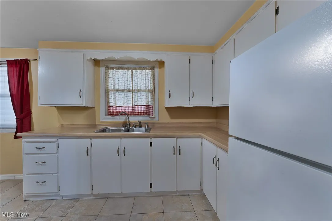 Kitchen with freestanding refrigerator, a sink, light tile patterned floors, light countertops, and white cabinets
