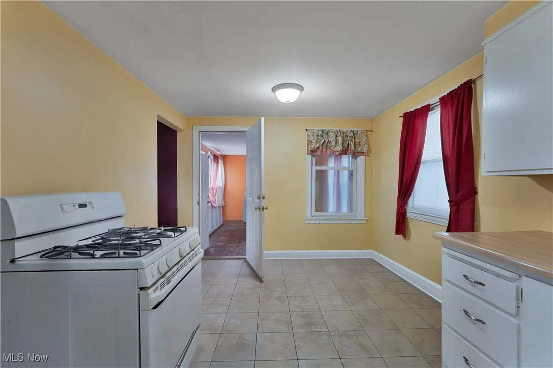 Kitchen featuring gas range gas stove, white cabinets, baseboards, light countertops, and light tile patterned flooring
