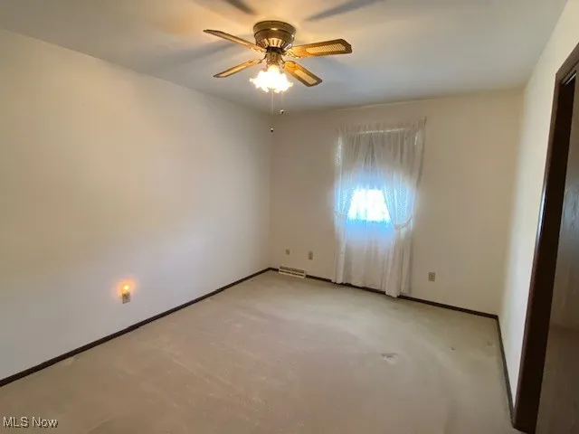 Empty room with ceiling fan, light carpet, and baseboards