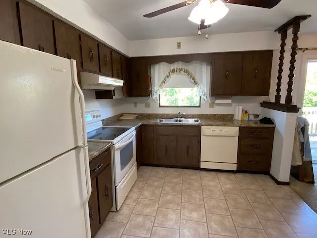 Kitchen featuring white appliances, under cabinet range hood, a sink, a ceiling fan, and dark brown cabinetry