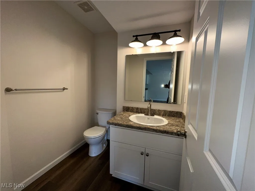 Half bathroom featuring LVT floors, toilet, baseboards, and vanity