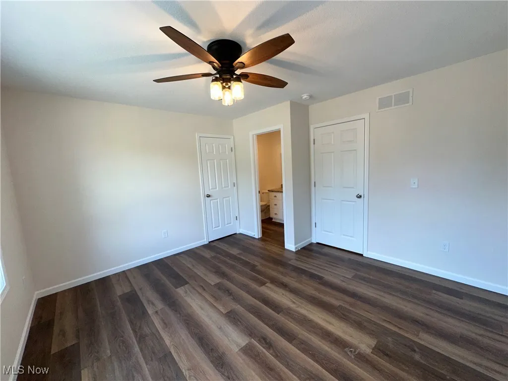 Unfurnished bedroom featuring baseboards, dark LVT flooring, and a ceiling fan