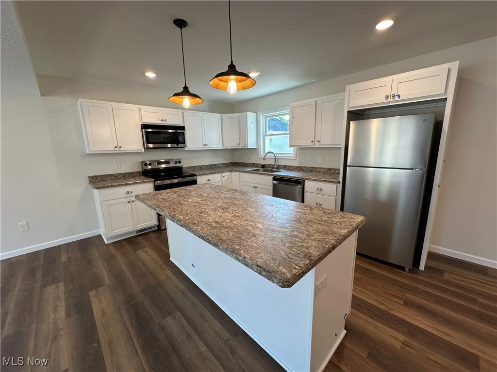 Kitchen with appliances with stainless steel finishes, a sink, baseboards, recessed lighting, and white cabinetry