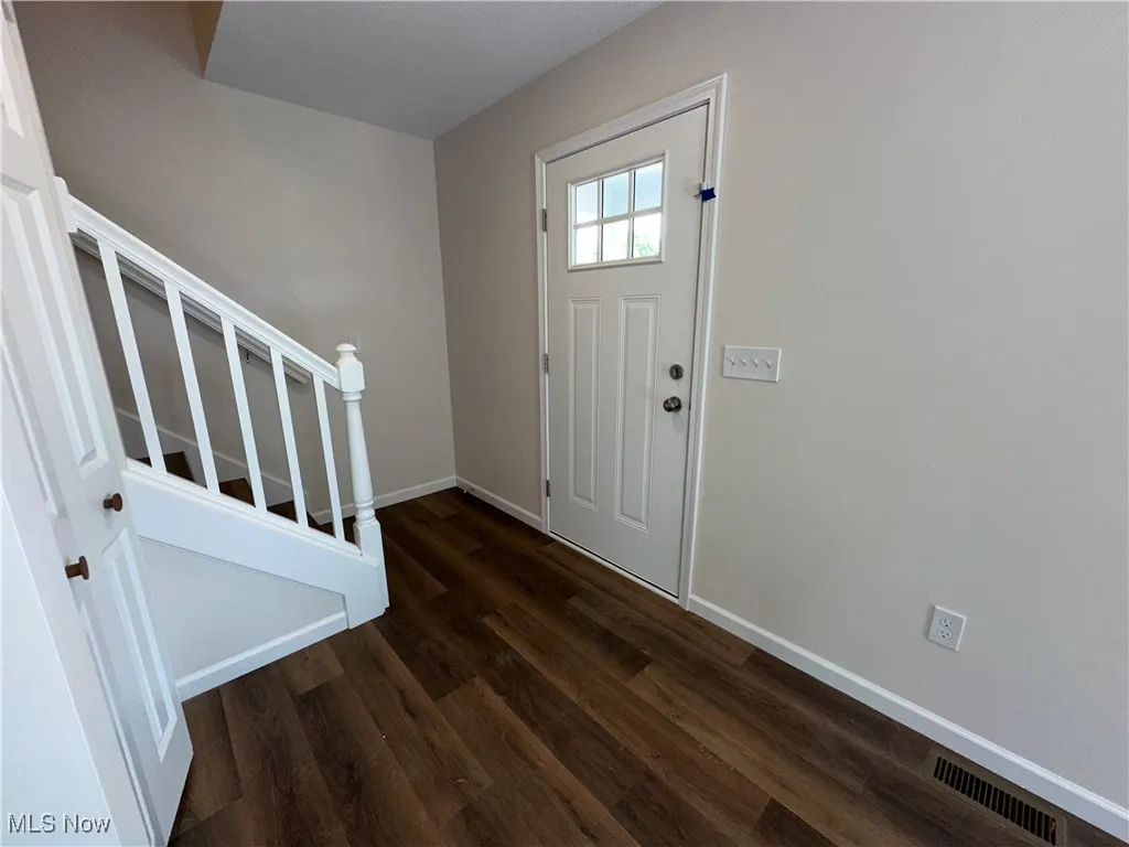 Foyer entrance with stairway, dark LVT floors, and baseboards