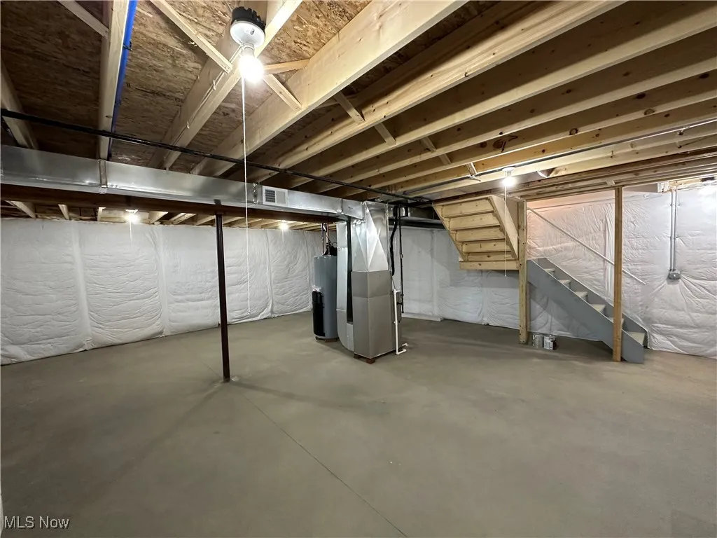 Unfinished basement with heating unit, water heater, and stairs