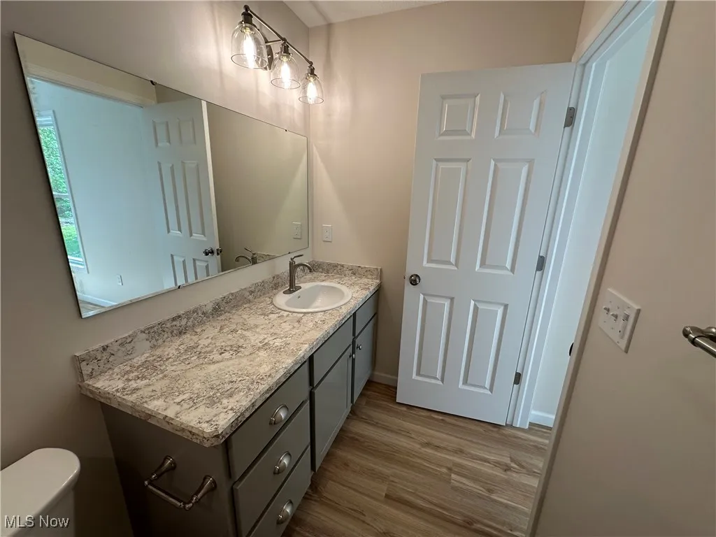 Bathroom featuring LVT floors, vanity, toilet, and baseboards