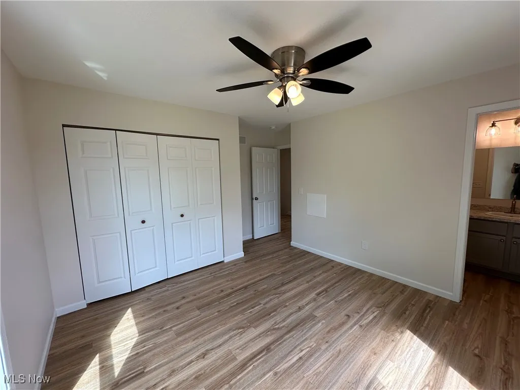 Unfurnished bedroom with light LVT flooring, baseboards, a closet, and a full bathroom