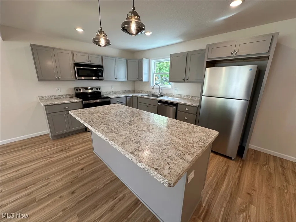Kitchen featuring appliances with stainless steel finishes, gray cabinets, a sink, baseboards, and light LVT floors