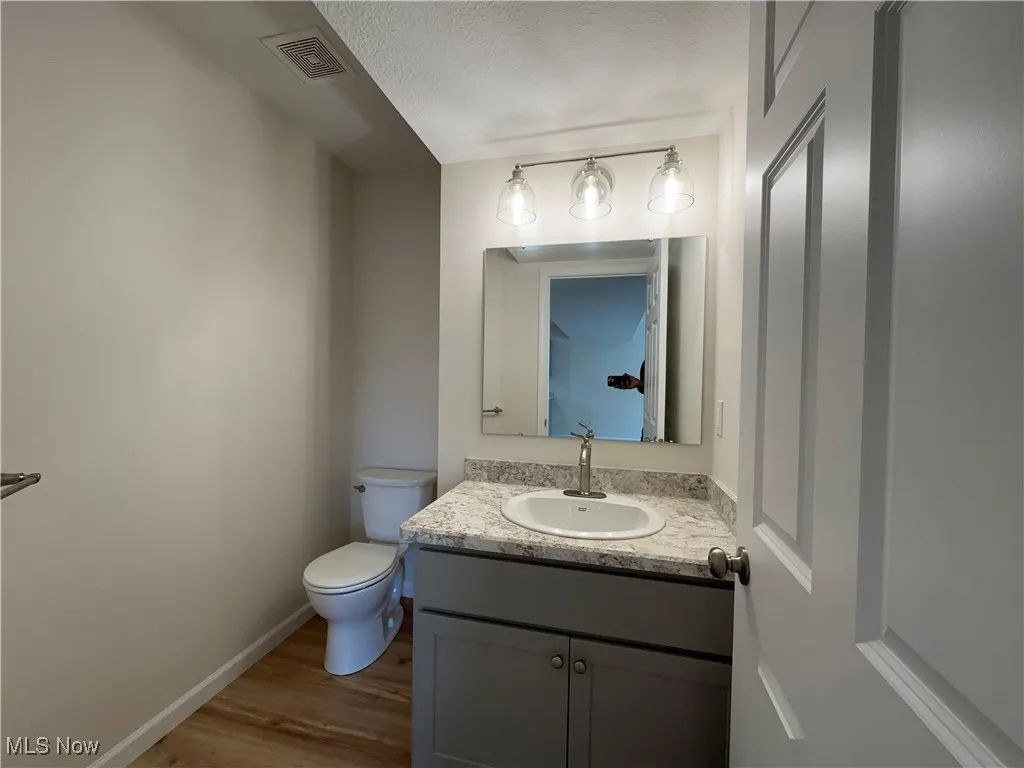 Half bathroom with LVT floors, baseboards, toilet, vanity, and a textured ceiling