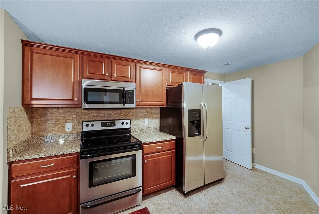Kitchen with stainless steel appliances, backsplash, baseboards, light stone countertops, and a textured ceiling