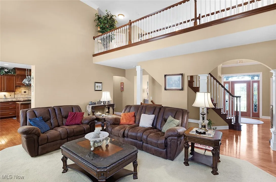 Living area featuring a high ceiling, arched walkways, light wood-type flooring, ornate columns, and stairway