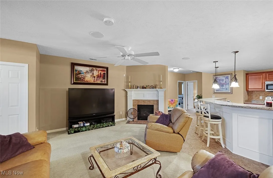 Living area with light carpet, a fireplace with flush hearth, a textured ceiling, a ceiling fan, and baseboards