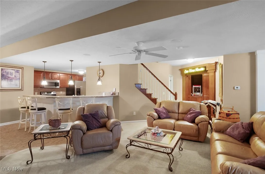 Living room with light colored carpet, stairway, baseboards, and a ceiling fan