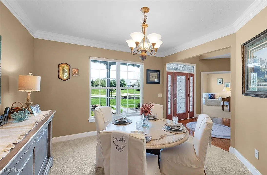 Dining room featuring a chandelier, light carpet, crown molding, and baseboards