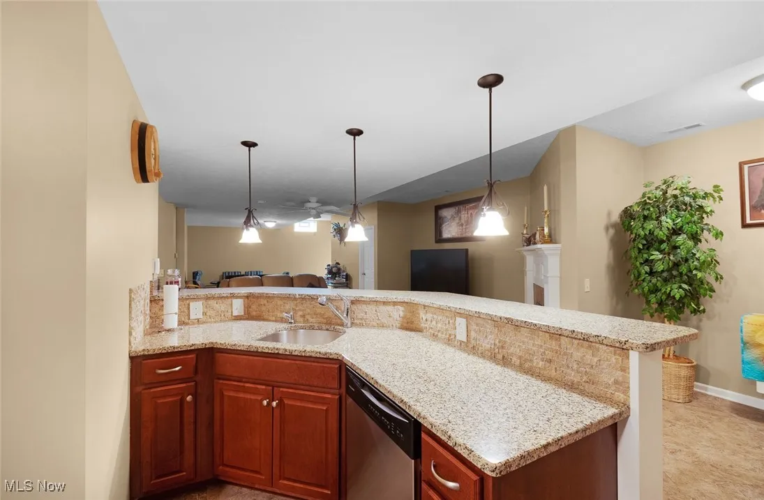 Kitchen with stainless steel dishwasher, a sink, open floor plan, light stone counters, and decorative light fixtures