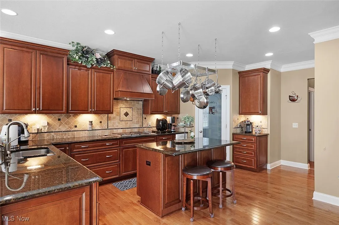 Kitchen featuring a sink, custom range hood, light wood-type flooring, stainless steel gas cooktop, and baseboards