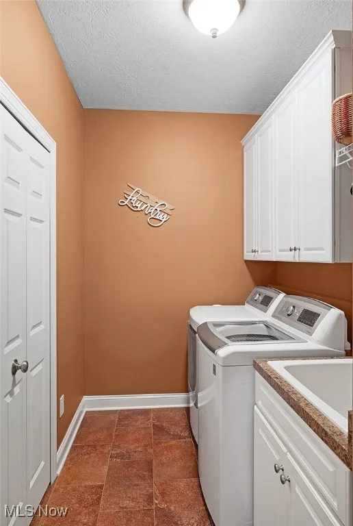 Washroom featuring separate washer and dryer, cabinet space, baseboards, and a textured ceiling