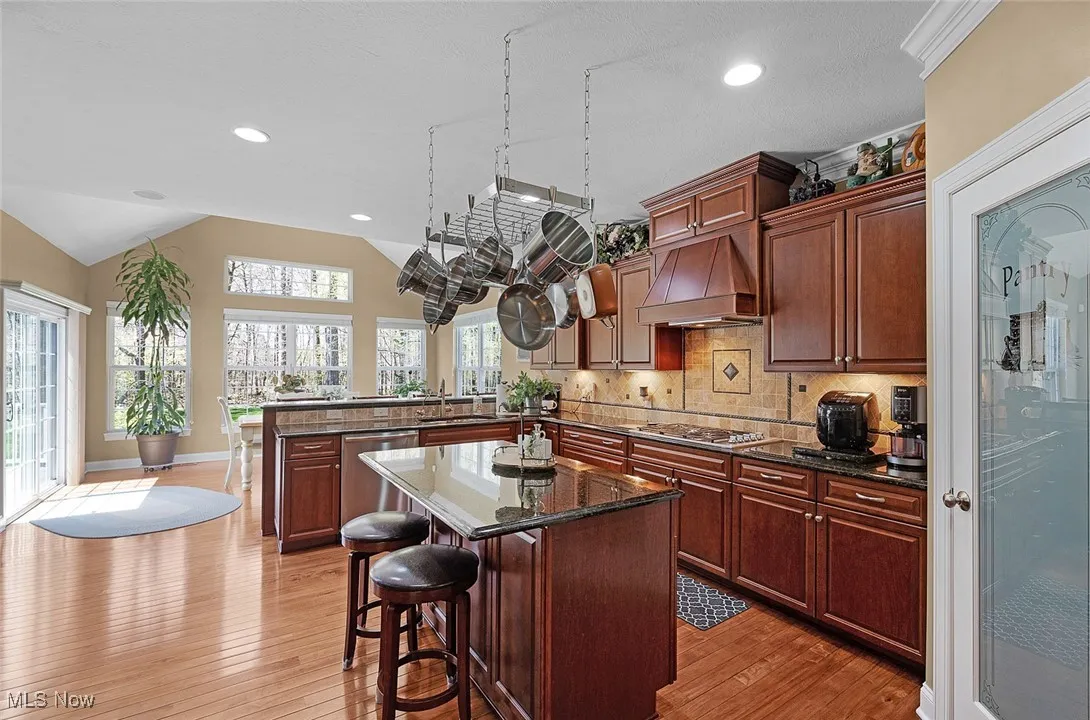 Kitchen featuring premium range hood, stainless steel appliances, a peninsula, light wood-style floors, and vaulted ceiling