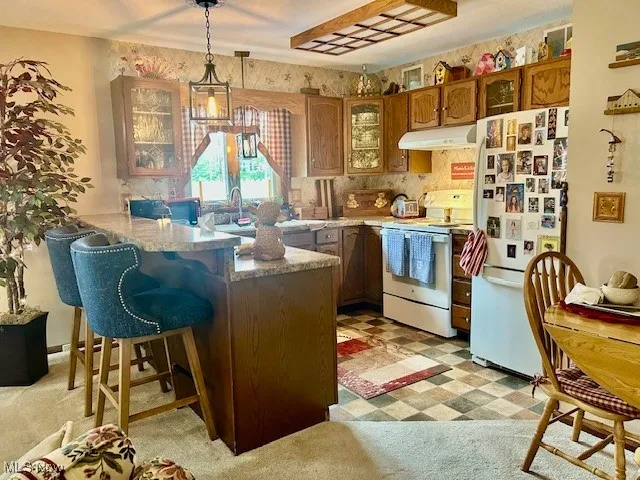 Kitchen featuring white appliances, under cabinet range hood, leaded glass insert cabinets. Overhead lighting and additional table area.