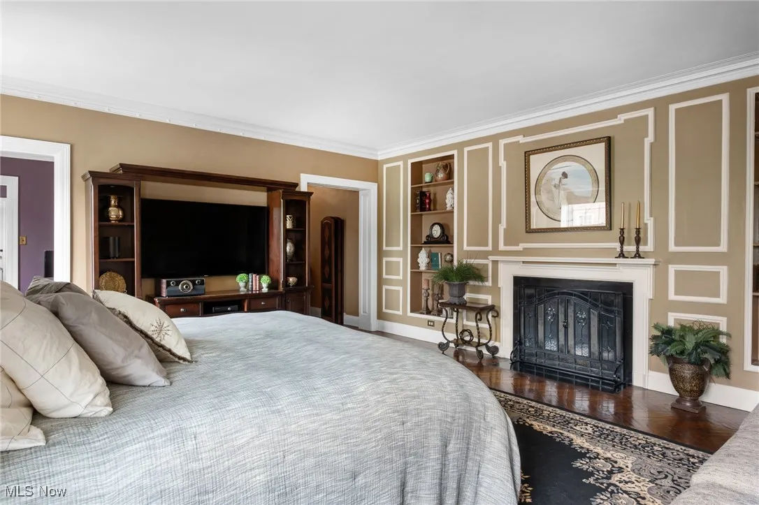 Bedroom with a fireplace, ornamental molding, and wood finished floors