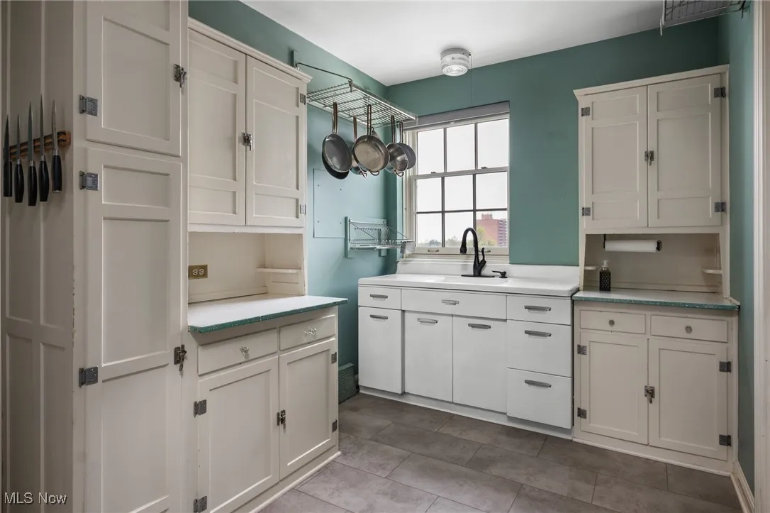 Kitchen with a sink, tile patterned flooring, light countertops, and white cabinets