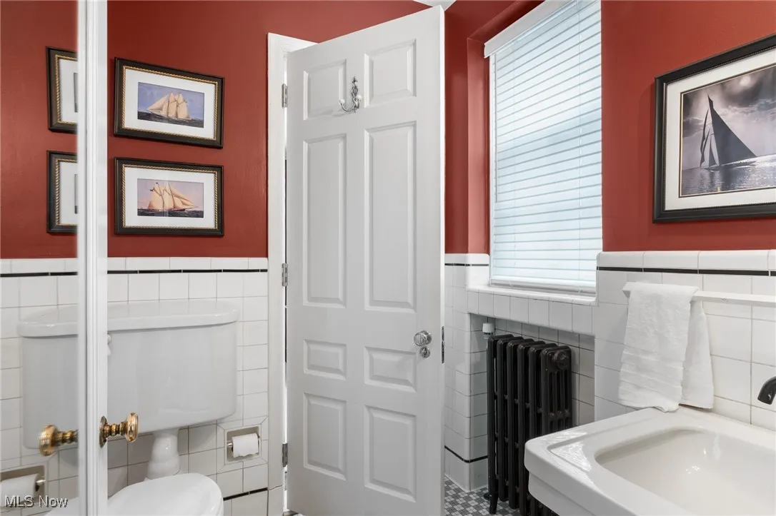 Bathroom with toilet, tile walls, radiator, and a wainscoted wall