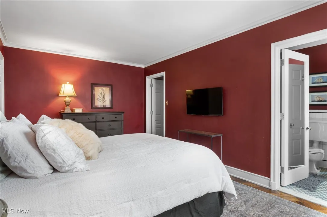 Bedroom with connected bathroom, wood finished floors, baseboards, and ornamental molding