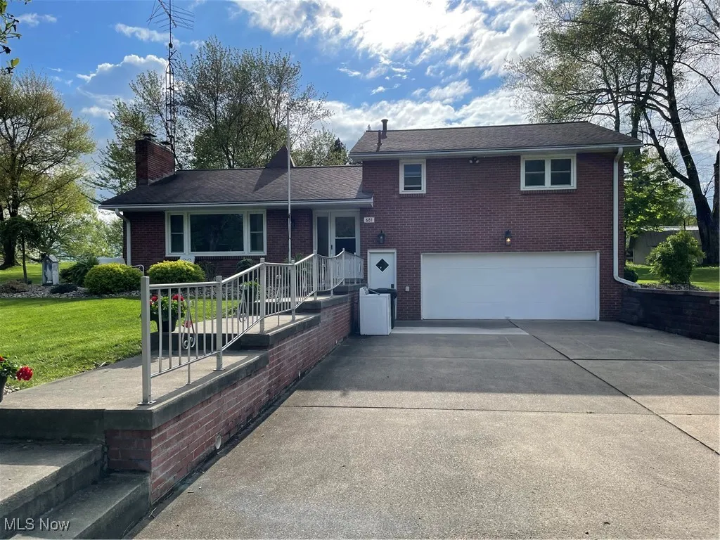 Split level home with a garage, driveway, a chimney, brick siding, and a front lawn