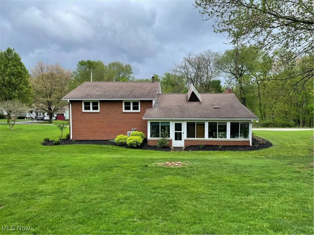 Back of property featuring a yard, brick siding, roof with shingles, and a chimney