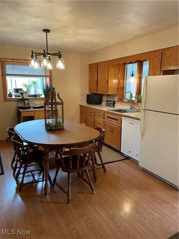 Kitchen with refrigerator, dishwashing machine, light wood-style floors, a sink, and brown cabinetry
