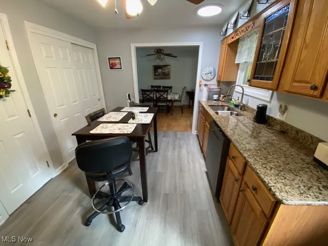 Kitchen with a sink, dishwasher, brown cabinets, wood finished floors, and ceiling fan
