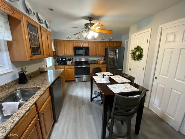 Kitchen with black appliances, brown cabinetry, light wood finished floors, and glass insert cabinets