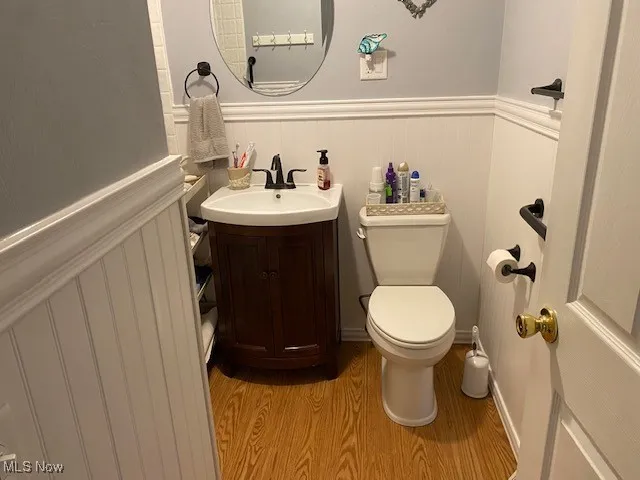 Half bath with wood finished floors, toilet, wainscoting, and vanity